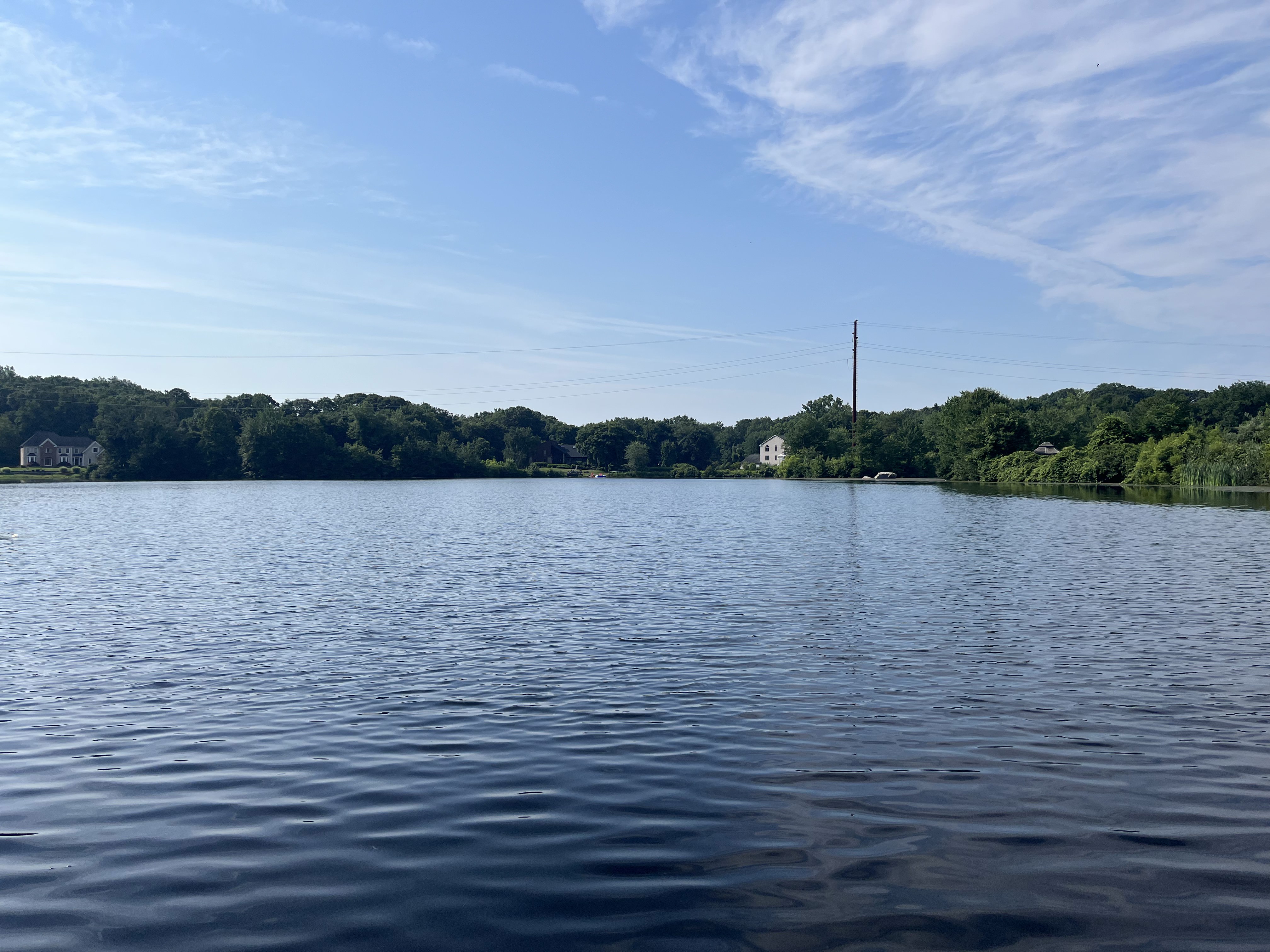 Landscape image of Fence Rock Lake. A blue lake surrounded by green trees and vegetation with a blue sky with some clouds.
