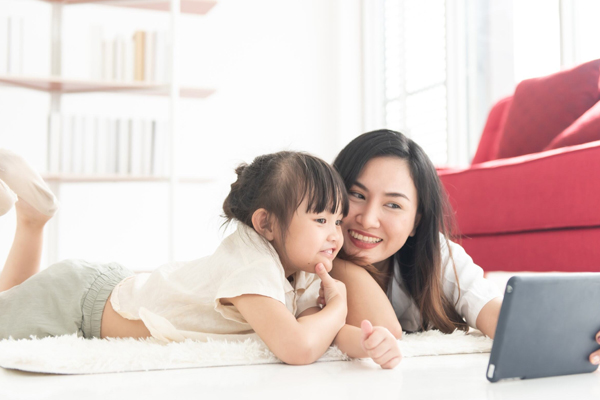 Mother and daughter lie on floor of house looking at tablet