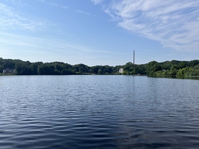 Landscape image of Fence Rock Lake. A blue lake surrounded by green trees and vegetation with a blue sky with some clouds.