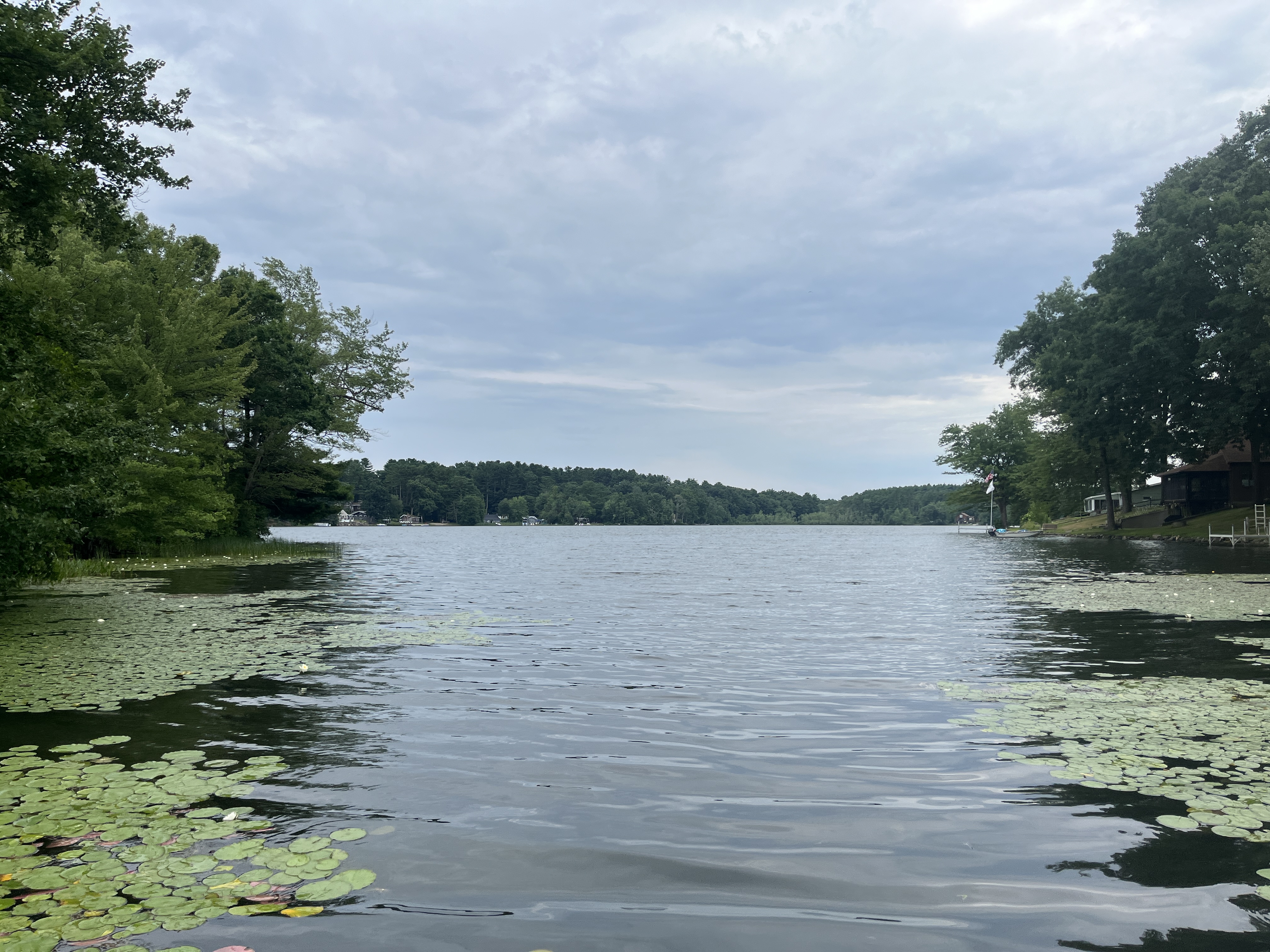 Landscape photo of Little Pond in Thompson, CT.  The water has lily pads on the edges and opens up into a larger lake with blue sky and trees on the shoreline.