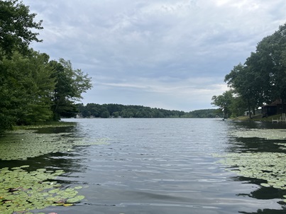 Landscape photo of Little Pond in Thompson, CT. The water has lily pads on the edges and opens up into a larger lake with blue sky and trees on the shoreline.