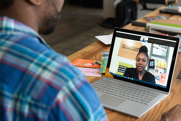 Black man in front of computer screen on desk in front of conference call.