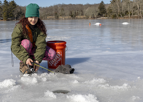 A young woman ice fishing on a lake in Connecticut.