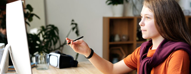 young girl wearing an orange shirt is using a computer to do research